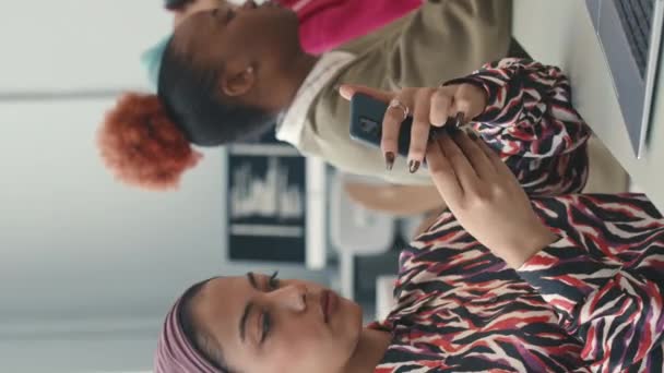 在明亮的办公室与多种族程序员一起工作时使用智能手机的年轻穆斯林妇女的垂直照片 — 图库视频影像