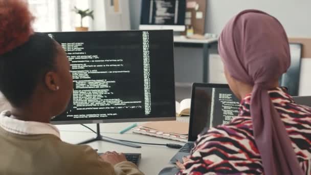 明るい現代オフィスでコンピュータ上でプログラミングしながらチャットする2人の多民族女性プログラマのバックビュー — ストック動画