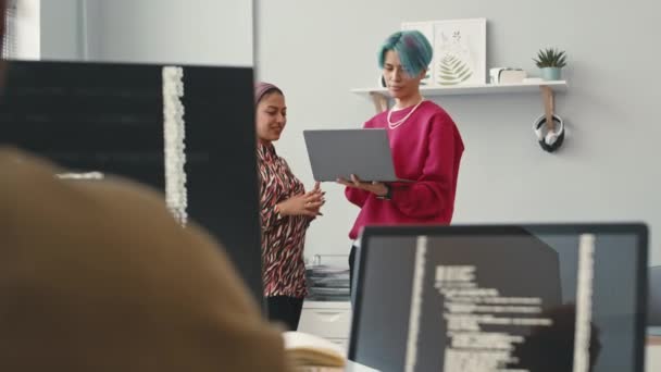 若いマルチテクノロジーソフトウェアエンジニアは ノートパソコンの画面を見て 現代のオフィスで同僚をしながらチャット — ストック動画