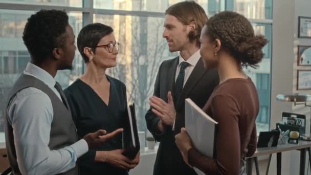 会話を持つ大きな窓を持つ現代のオフィスに立っている4人のプロの多民族弁護士の中型ショット — ストック動画