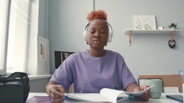 ワイヤレスヘッドフォンでアフリカ系アメリカ人女性It学生のPovを待ってカメラを見て 屋内学習教材の机に座って話す — ストック動画