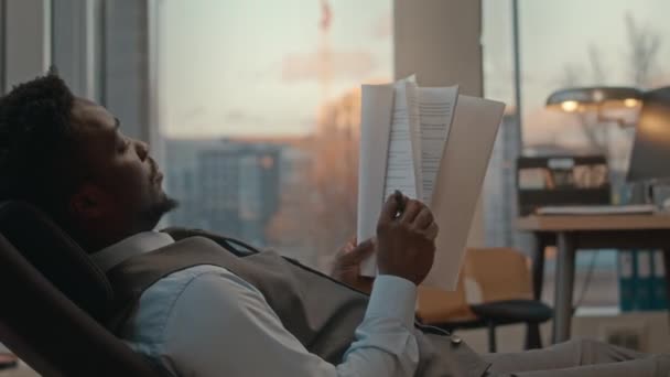 アフリカ系アメリカ人のビジネスマンは 高級オフィスのソファーで休憩し パノラマウィンドウを読み ビジネス契約でメモを作ります — ストック動画