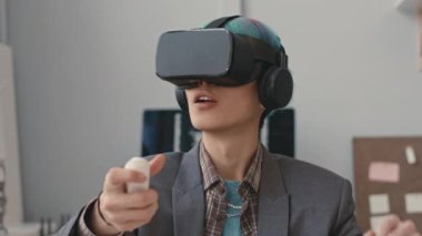 VR kulaklıklı, ofisteki kumandayı kullanarak sanal oyun oynayan konsantre Asyalı adam.