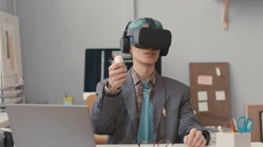 Genç Asyalı erkek yazılım mühendisinin kemeri VR kulaklık takıyor ve ofiste çalışırken kontrol mekanizması çalışıyor.