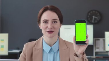 Beyaz tenli genç iş kadınının göğsünü kabart ve kameraya yeşil şablon akıllı telefon ekranı göster.