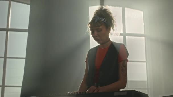 在阳光照射下的工作室里 白人年轻纹身女子在键盘上弹奏摇滚音乐的中景照片 — 图库视频影像