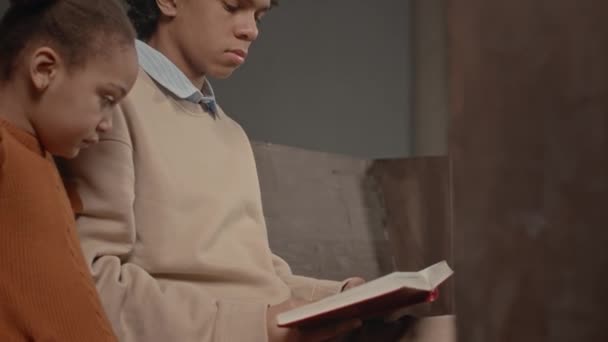 童年时代的男孩 带着妹妹坐在木制长椅上 在天主教堂读圣经 — 图库视频影像