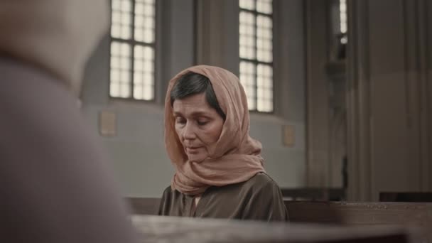 周日礼拜时 在天主教堂的木制长椅上 用头巾为成熟的白人妇女祈祷 — 图库视频影像