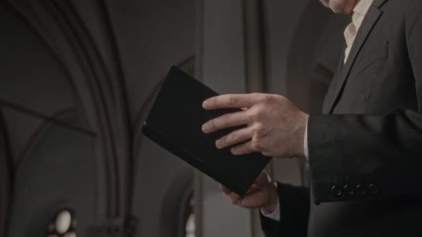 无法辨认的牧师手拿着圣经在教堂典雅的黑色斗篷上的布景 — 图库视频影像