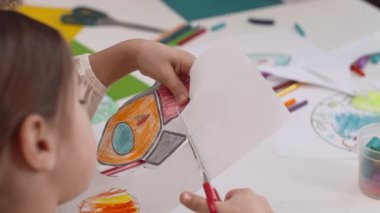 Anaokulu kızı sınıfta el işi yaparken uzay roketinin fotoğrafını kesiyor.
