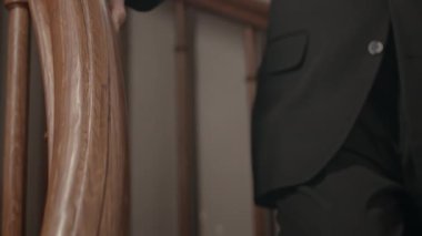 Kilisedeki ahşap merdiven korkuluğuna elini dayayan, takım elbiseli, tanınmamış Katolik rahibin yakın çekimi.