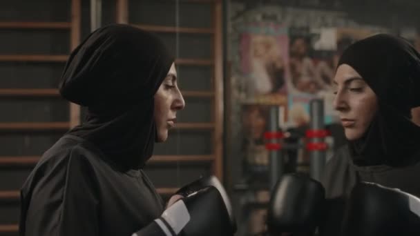 穿着黑色头巾和拳击手套站在地下拳击俱乐部镜子前练习拳击的年轻穆斯林妇女 — 图库视频影像
