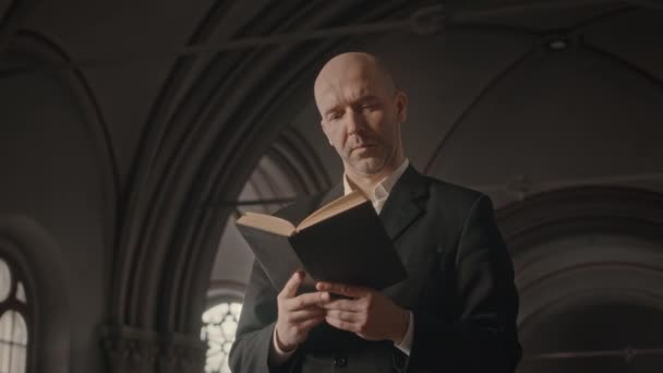 カトリック教会での奉仕中にホーリーブックを読んで司祭を率いたハゲのミディアムショット — ストック動画