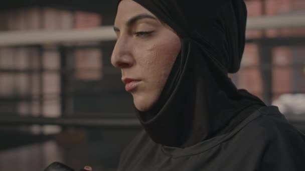 在黑暗俱乐部接受拳击训练的同时 紧紧围绕着有信心的年轻穆斯林女子在头巾打拳袋时的动作 — 图库视频影像