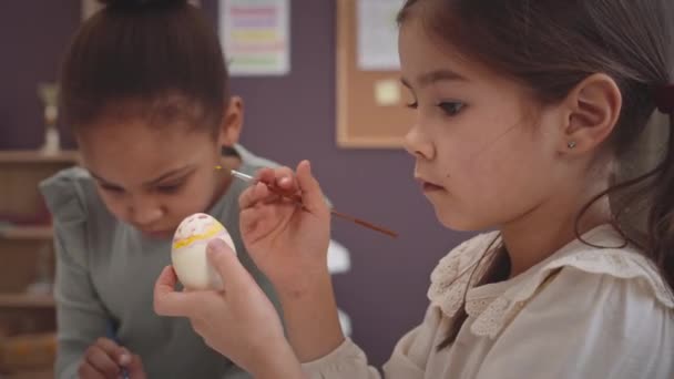 イースターエッグを絵画し 学校で一緒に装飾をする2つの小さい年齢の多民族少女 — ストック動画