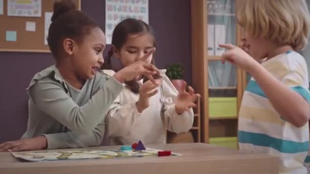 在现代教室里玩骰子玩棋盘游戏的同时 养育着三个快乐多样的一年级学生 — 图库视频影像