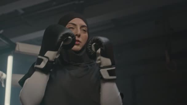 在拳击俱乐部用打斗袋进行头巾训练的穆斯林女子低角度射击 — 图库视频影像