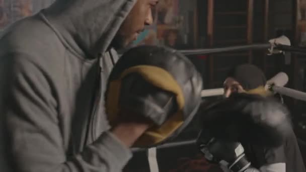 年轻的穆斯林妇女与黑人男子教练在室内拳击台上练习拳击 — 图库视频影像