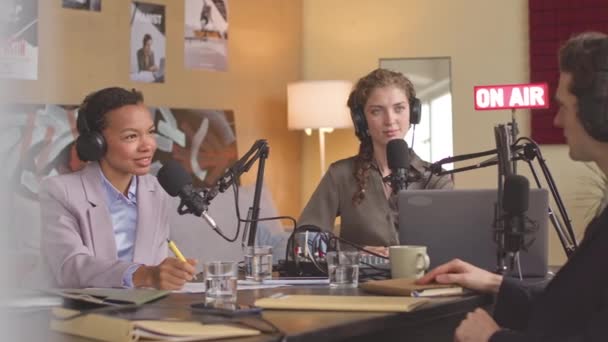 在专业的广播演播室里 一对多种族的商业伙伴和年轻的女电台主持人坐在他们的麦克风旁 就商业话题录制播客 — 图库视频影像