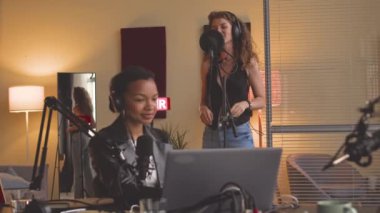 İki farklı genç kadın ses stüdyosunda profesyonel ekipman kullanarak şarkı kaydediyor.
