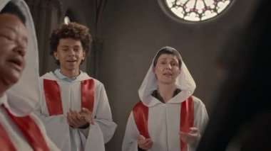 Hıristiyan kilise korosunun çok ırklı üyeleri beyaz elbiseler giyip birlikte şarkı söylüyorlar.