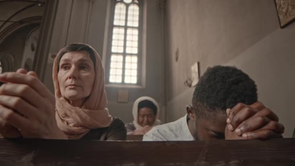 在天主教堂的木制长椅上排成一排的多种族教区居民一边祈祷一边祈祷 — 图库视频影像