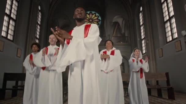 カトリック教会でのパフォーマンス中に歌うために白いガウンを身に着けている多民族教会合唱団のショットでズーム — ストック動画
