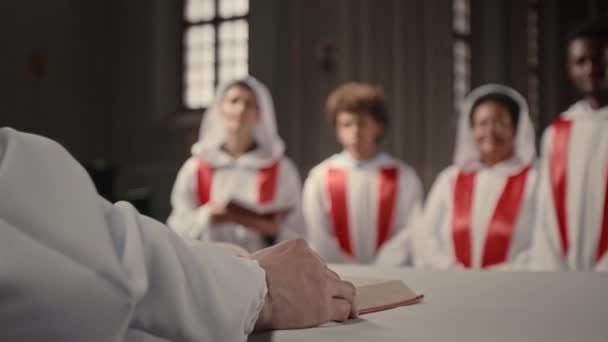 認識できない男性司祭は 長い白いガウンを身に着けている教会合唱団の多様なメンバーに話します — ストック動画