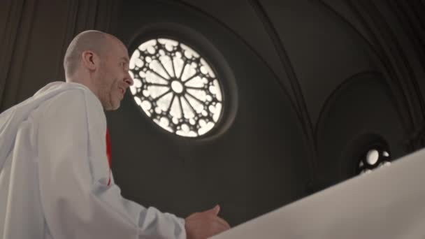 古いカトリック教会で説教する白いガウンの中年白人男性司祭の低い角度 — ストック動画