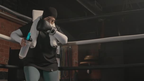 年轻的穆斯林女拳击手在打完架后站在拳击台角落休息 — 图库视频影像