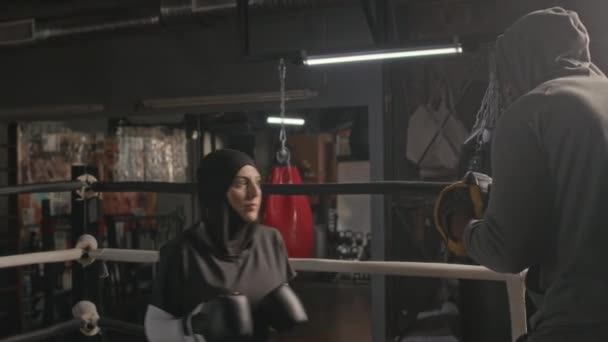年轻的穆斯林女子身穿黑色头巾和运动服 在室内拳击赛训练中与她的黑人教练打斗 — 图库视频影像