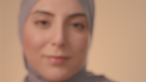 放大极近的画像年轻的棕色眼睛的穆斯林妇女在头巾看着相机站在油桃工作室的背景 — 图库视频影像