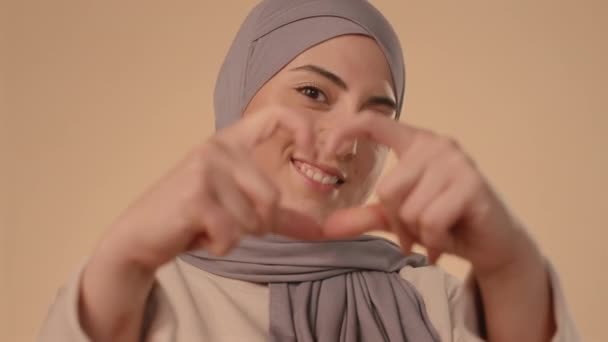 在工作室里 戴着头巾的年轻穆斯林妇女手牵着手 对着镜头微笑 站在红桃背景上 — 图库视频影像