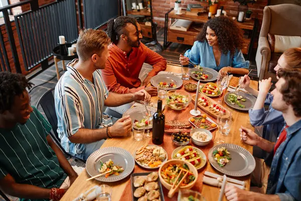 在舒适的环境中 不同类型的年轻人在餐桌边享用晚餐时的高透视 — 图库照片