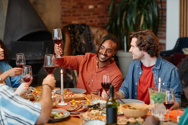 在与朋友们共进午餐时 在舒适的氛围中 一个面带微笑的黑人男子与酒杯敬酒的画像 — 图库照片