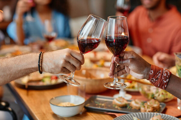 Close up of two people clinking wine glasses during dinner party in cozy setting, copy space