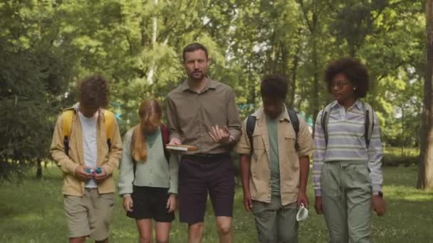 屋外遠足の間に公園エリアを探索する多文化小学生のグループと白人男性教師の中型ショット — ストック動画