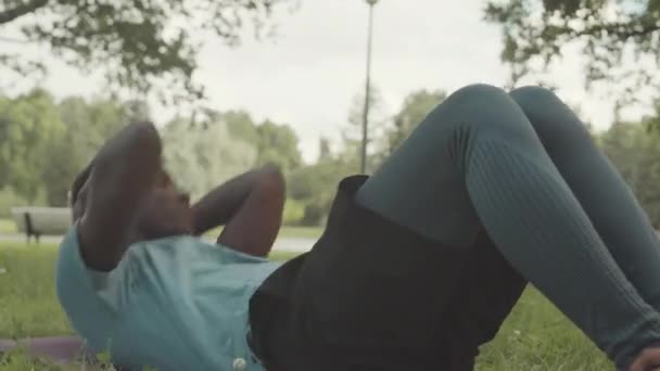 若い運動黒人の男は暖かい晴れた日の公共の公園の屋外のトレーニングの間にクランチをします — ストック動画