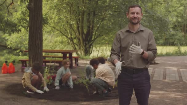 白种人男老师在公园与不同类型的儿童一起种植新植物时 戴着手套摆好姿势拍照的中速肖像 — 图库视频影像