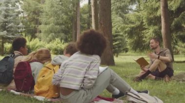 Kafkas erkek öğretmen, parktaki yeşil çimlerin üzerinde oturan bir grup çok ırklı öğrenciye ilginç bir hikaye anlatıyor.
