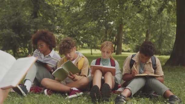 Groep Van Diverse Basisschoolkinderen Met Copybooks Hun Schoot Zittend Groen — Stockvideo