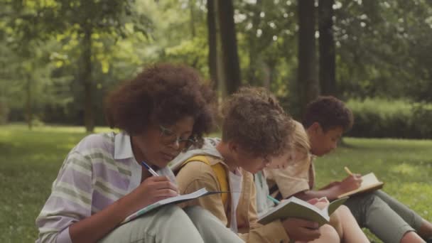 Niños Multiraciales Sentados Césped Parque Cálido Día Soleado Escribiendo Sus — Vídeos de Stock