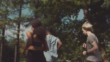 Yaz mevsiminde halka açık parkta birlikte koşan dört farklı erkek ve kadın arkadaşın orta geri görüşü.