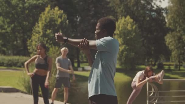 在阳光明媚的日子里 在公园进行户外活动前热身时 中镜头拍摄的年轻黑人男子展开胳膊和肩膀 — 图库视频影像