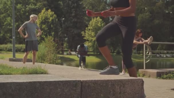 在阳光灿烂的日子里 与其他运动员一起在公园里进行户外运动时 体形匀称的年轻女子正在进行提速运动 — 图库视频影像
