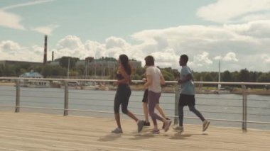 Sıcak güneşli bir günde köprü boyunca birlikte koşan dört formda genç sporcudan oluşan tam boy yavaşlama.