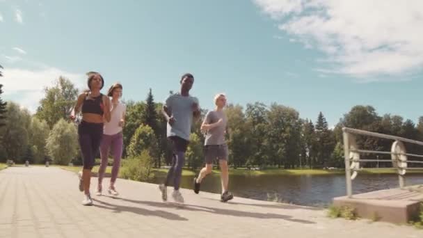 在温暖的阳光灿烂的日子里 四个年轻的男女运动员一起在人行道上跑步 全速前进 — 图库视频影像
