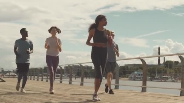 四名身穿运动服的年轻男女在阳光照射下沿着桥慢跑的全长镜头 — 图库视频影像