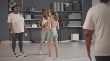 Parlak ferah stüdyoda grup fitness kursu sırasında sohbet eden üç genç kadının tam boy çekimi.