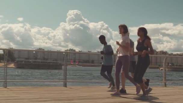 晴れた日の街遊歩道で一緒にジョギングする4人の多様な人々の完全な長さのスローモ — ストック動画